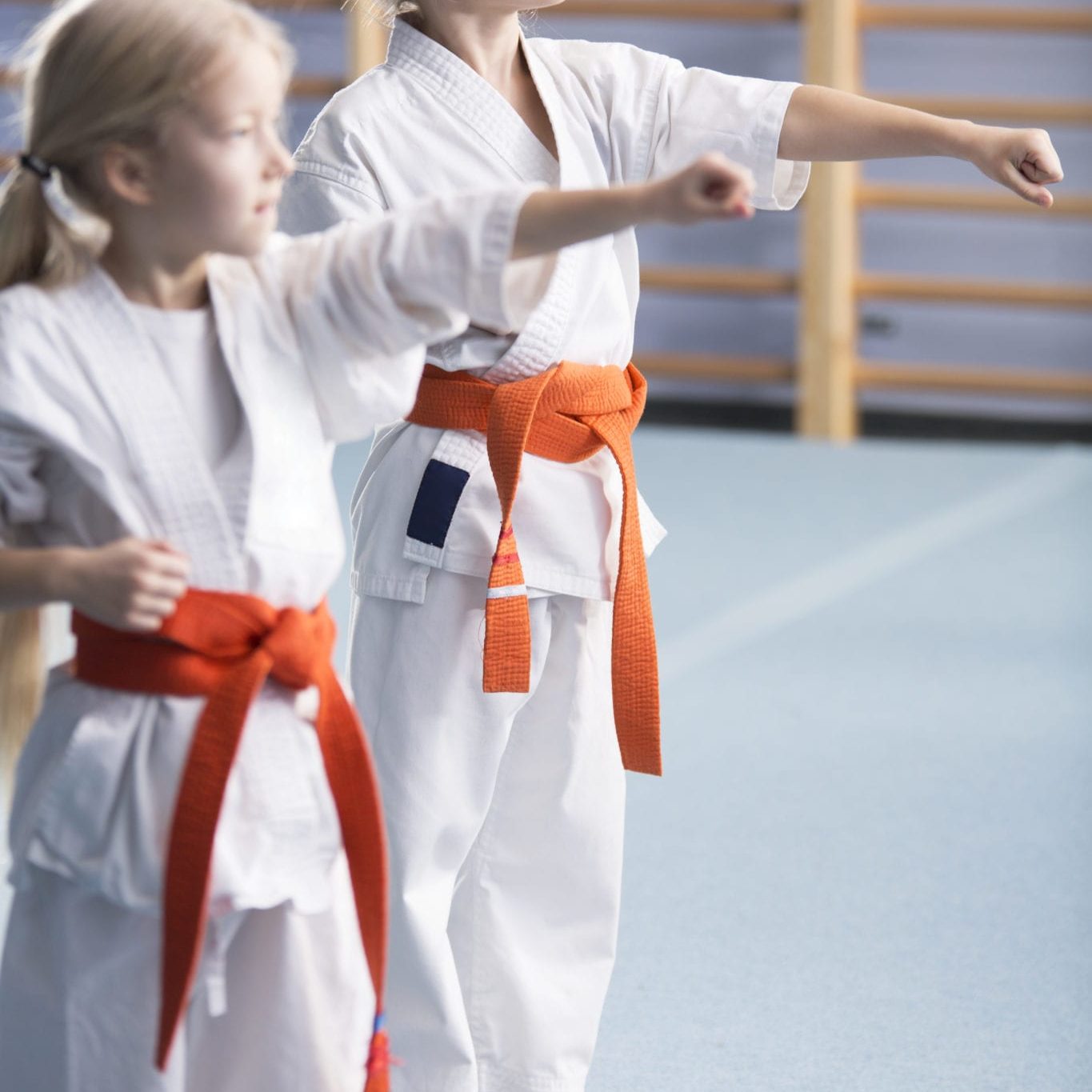 Young girls wearing orange belts, training moves and looking in the direction of their coach during karate classes